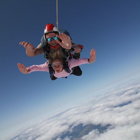 A women and man in the air doing a tandem skydive smiling