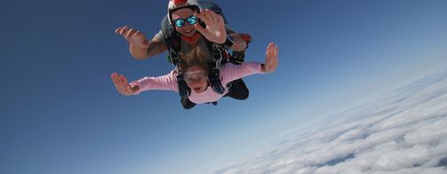 A women and man in the air doing a tandem skydive smiling