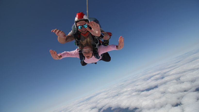 A women and man in the air doing a tandem skydive smiling