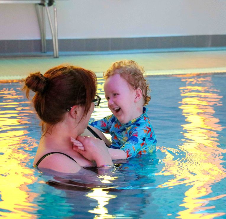 Little boy smiling lovingly at mum in pool