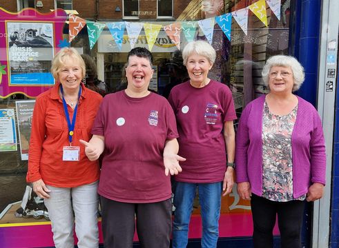 a team of charity shop volunteers smiling together in front of a window