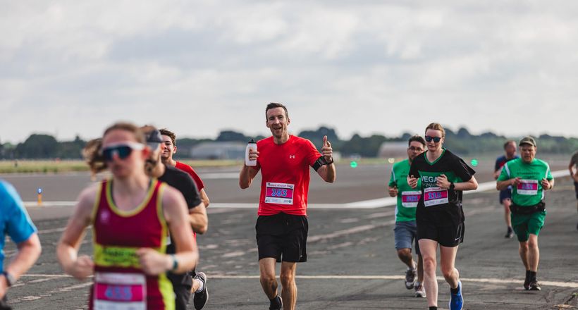 A man running on a runway with his thumbs up smiling